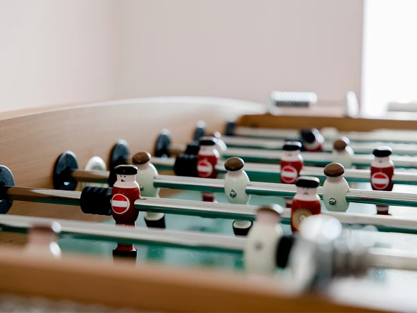 Ein Nahaufnahme eines Tischfußballs mit Figuren in rot und weiß, die auf Stangen montiert sind. Der Tisch hat eine Holzoberfläche und der Fokus liegt auf den Spielfiguren.