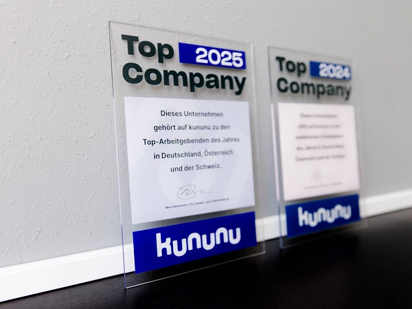 Zwei Auszeichnungen für das Unternehmen kununu, die als "Top Company 2025" ausgezeichnet wurden. Die Plaketten sind durchsichtige Acrylglasrahmen, die Text in blau und grün zeigen, sowie das Logo von kununu.